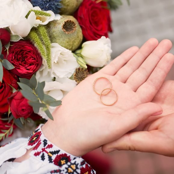 bride and groom hold wedding rings in their arms